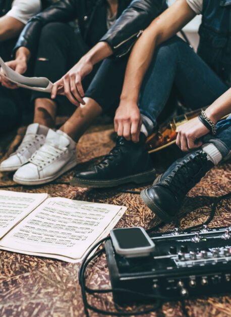 Repetition of rock music band. Cropped image of guitar players and drummer are sitting on the floor at rehearsal base with notes.